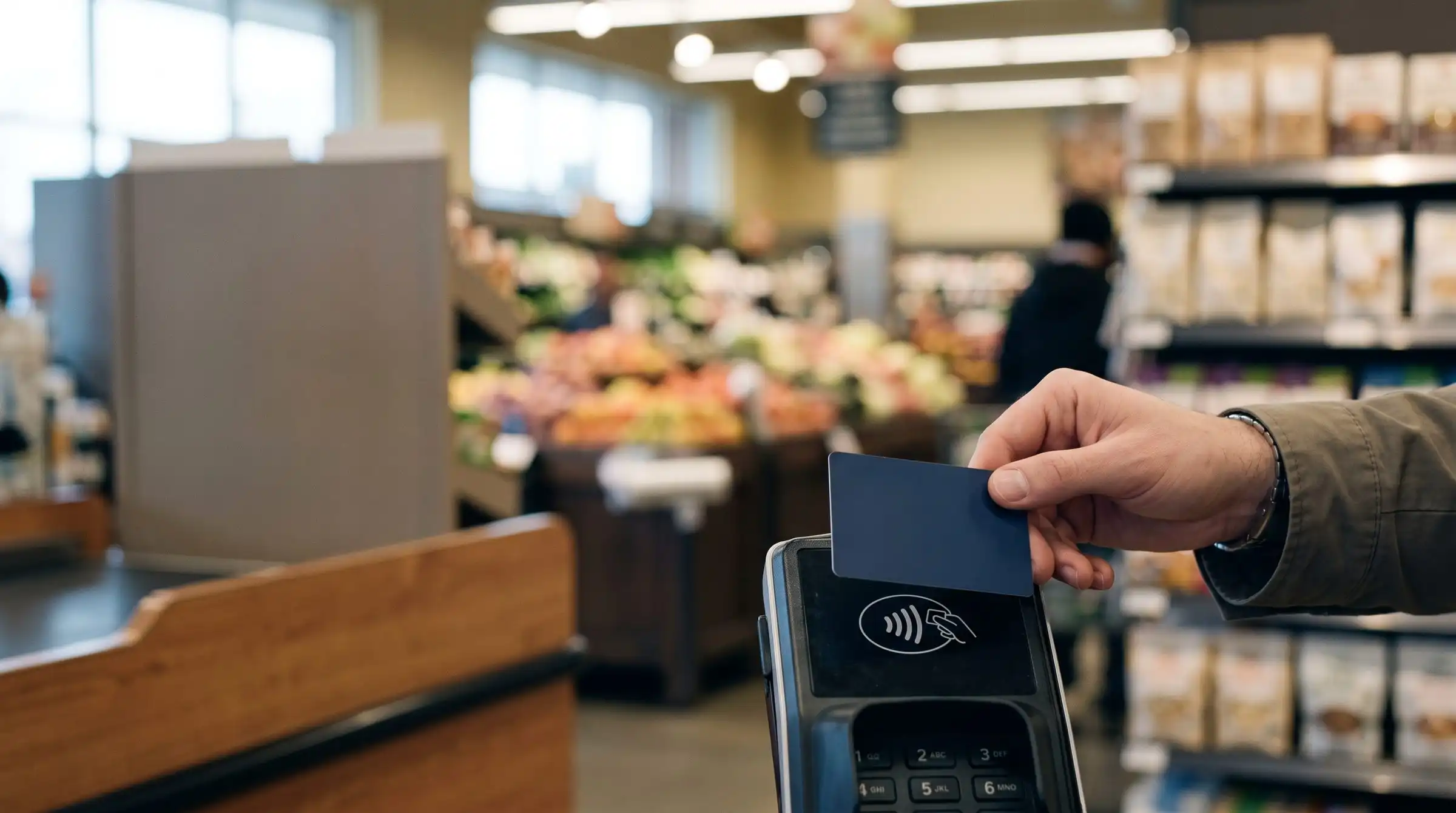 Hand tapping a payment card on a card reader at a grocery checkout